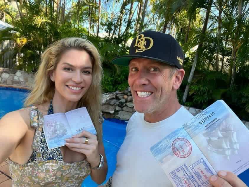 A woman and man stand in front of a pool with their passports which have a stamp from American Samoa.