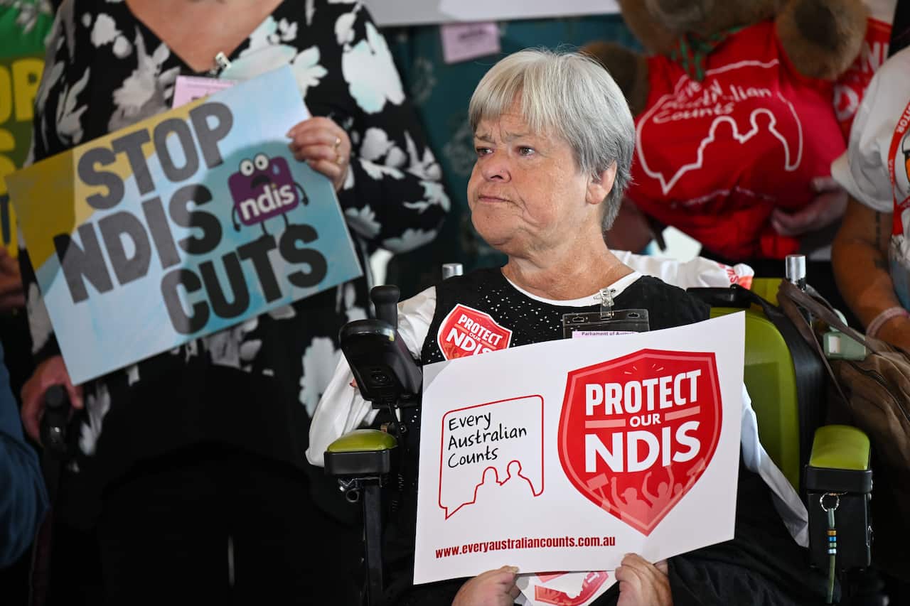 A woman holds a sign saying 'Protect our NDIS' at a media conference.