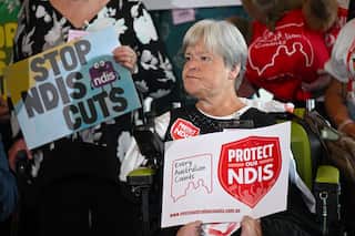 A woman holds a sign saying 'Protect our NDIS' at a media conference.