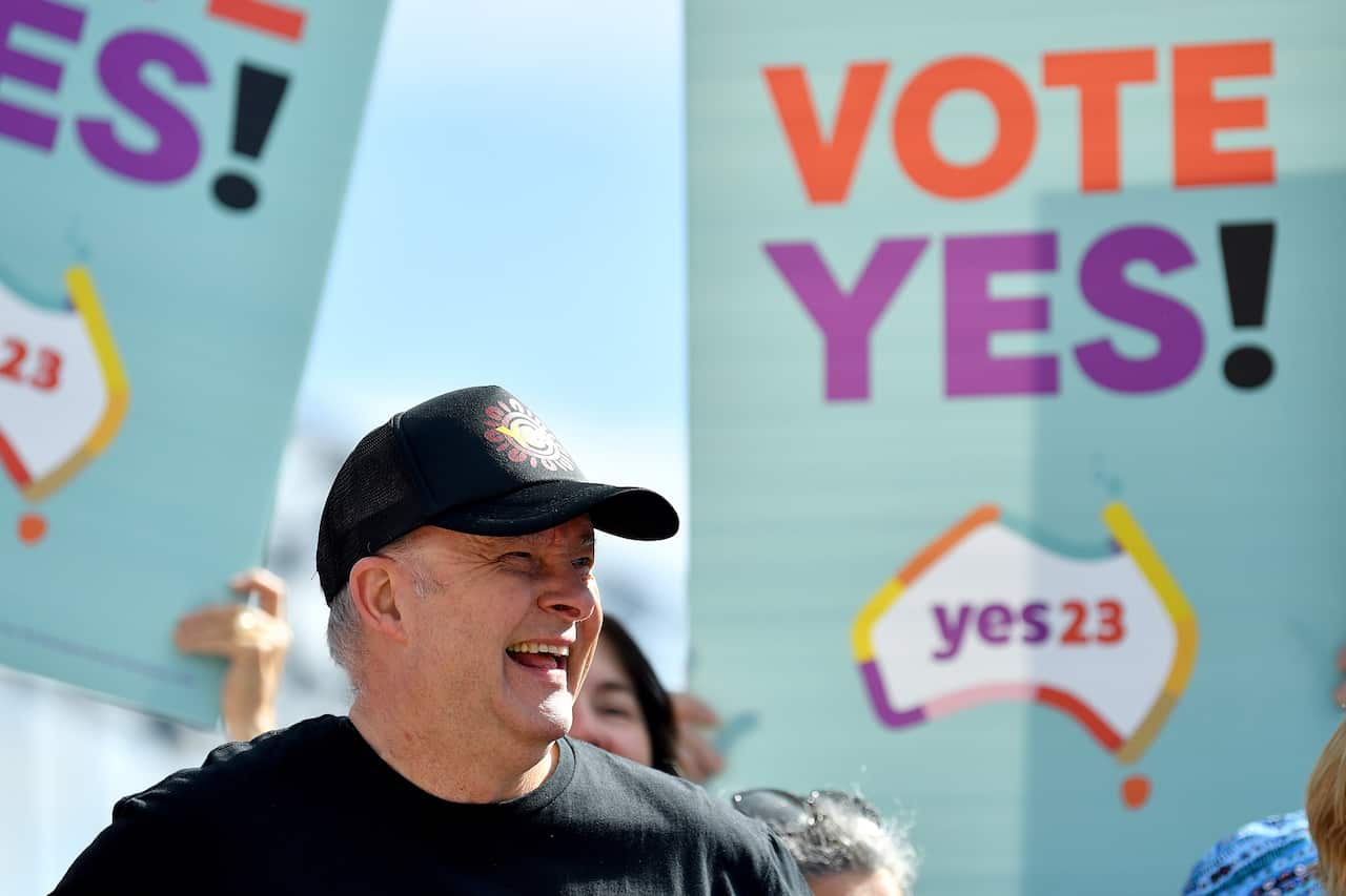 Man in cap smiles in front of Yes placards.