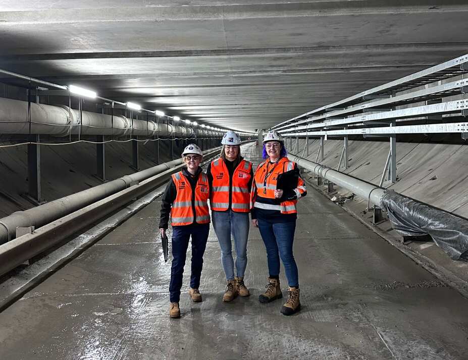 Three women wearing helmets, hi-vis vests and boots standing in a tunnel