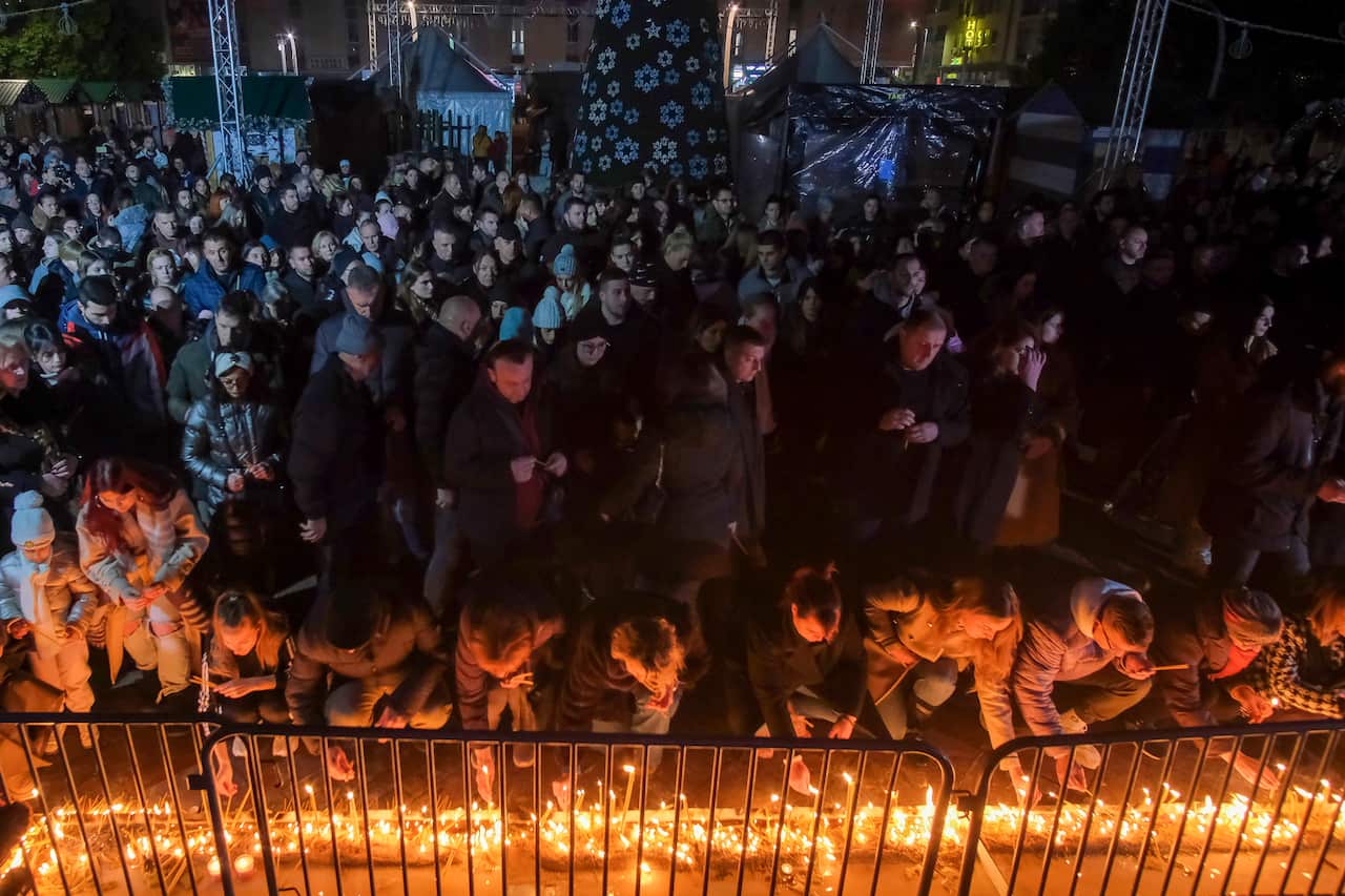 A large group of people standing together, with the front row kneeling and lighting candles.