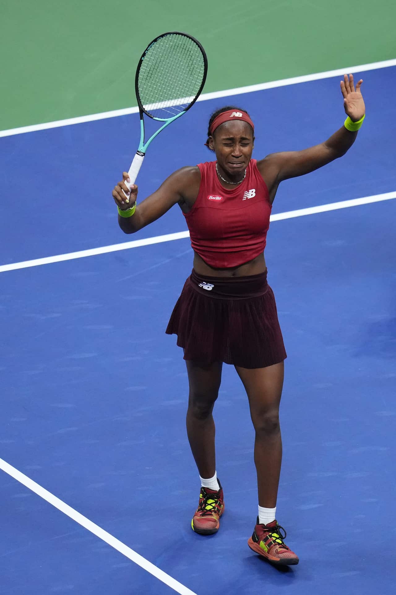 A woman in a tennis uniform crying and raising her racket