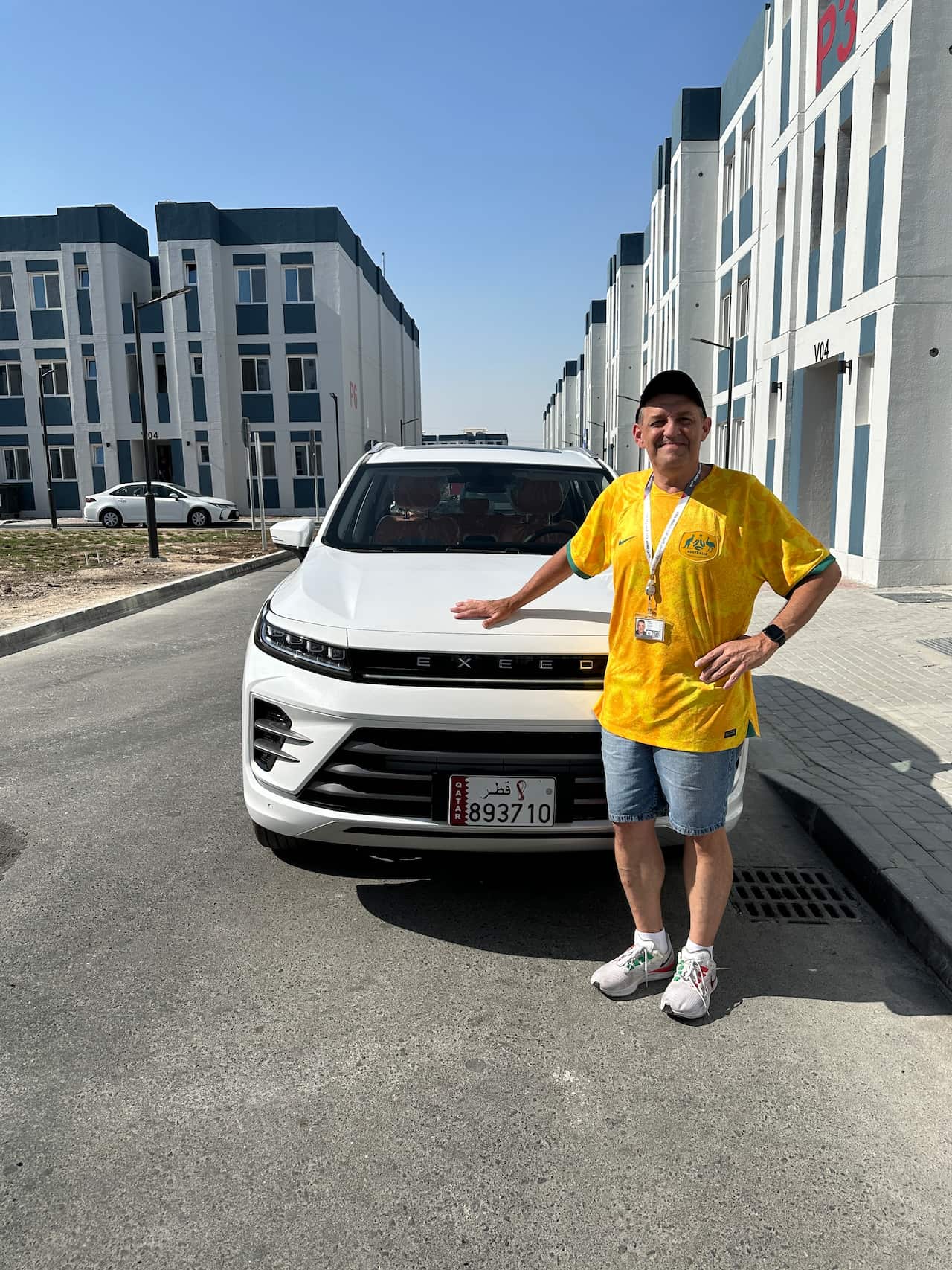 A man wearing a gold Australia football shirt is posing in front of a car