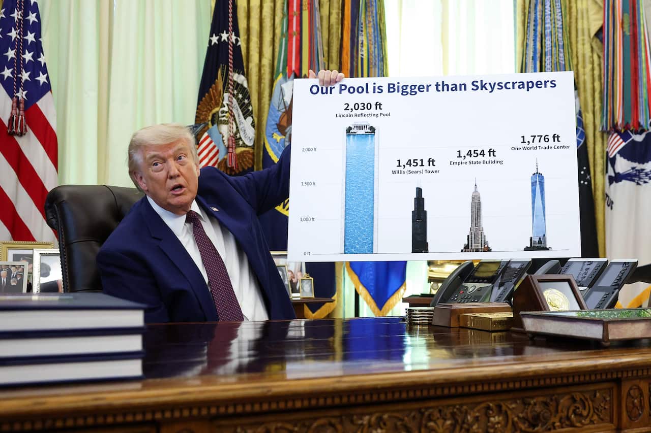 Donald Trump holds a sign that says "our pool is bigger than skyscrapers" in the Oval Office.