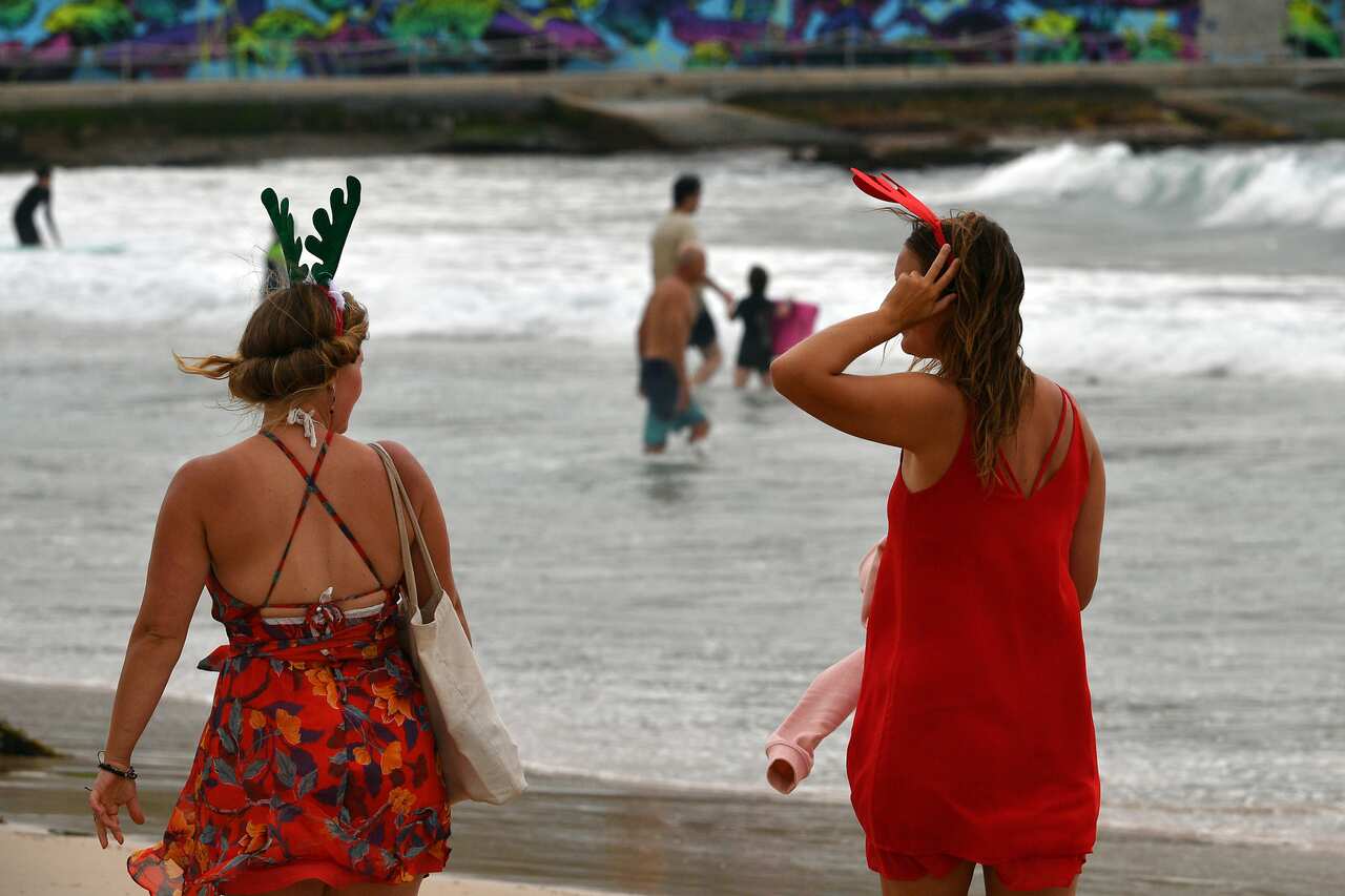 Two girls wearing antlers and dressed in red walk on a beach