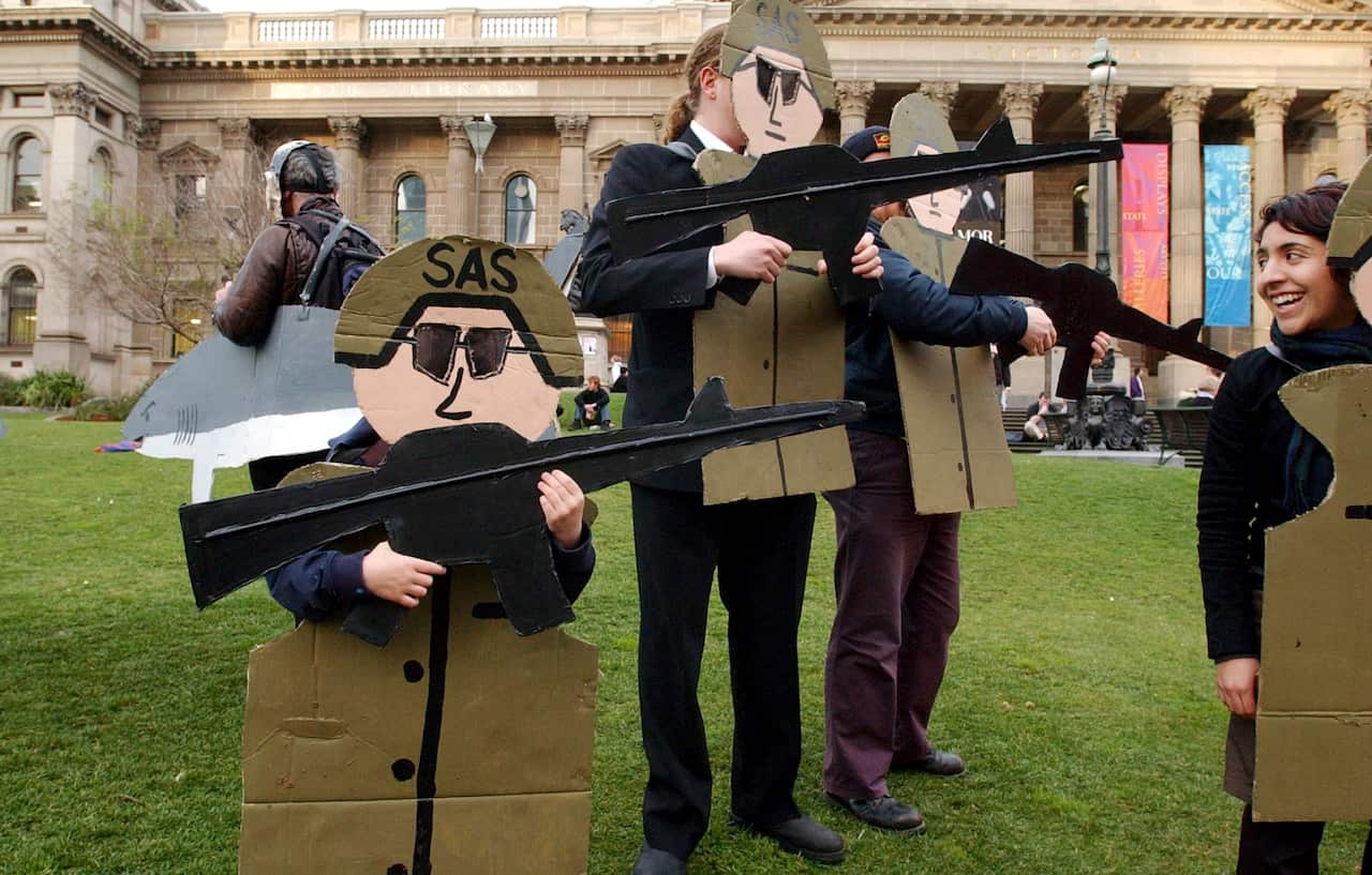 Protesters dressed in cardboard shirts and rifles stand outside a building.