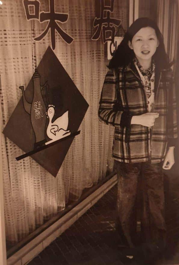  A black and white photo of a woman standing outside a Chinese restaurant.