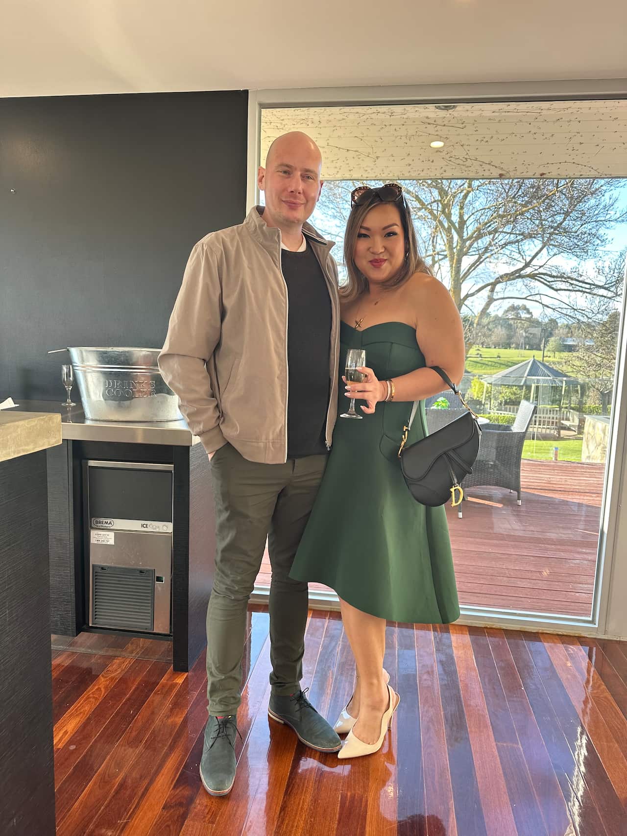 A Chinese woman wearing a green dress holds a glass of champagne while posing next to a man.