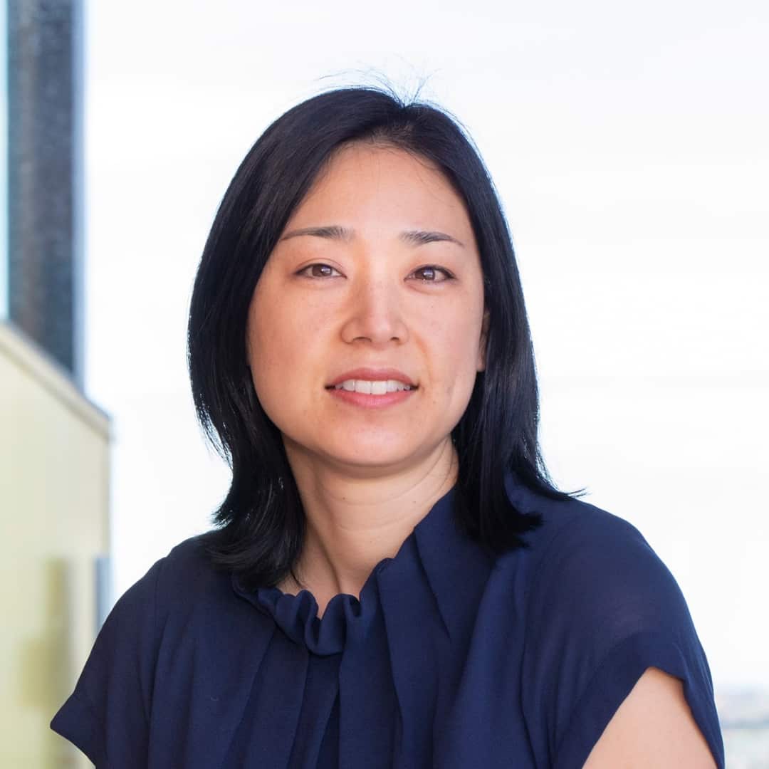 A woman with shoulder-length straight dark hair and a black top faces the camera