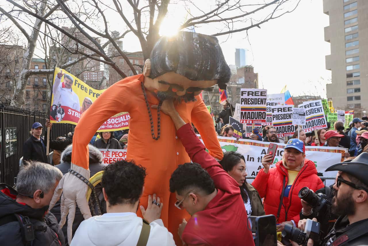 A group of people holding up an effigy of Nicolas Maduro in an orange jumpsuit. Protesters can be seen behind them holding signs that say "Free President Maduro".