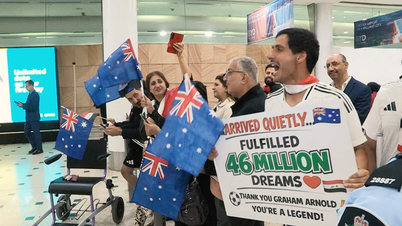 Fans at Sydney Airport wave Australian flags and hold a sign thanking Graham Arnold for fulfilling "46 million dreams" alongside a small Iraqi flag.