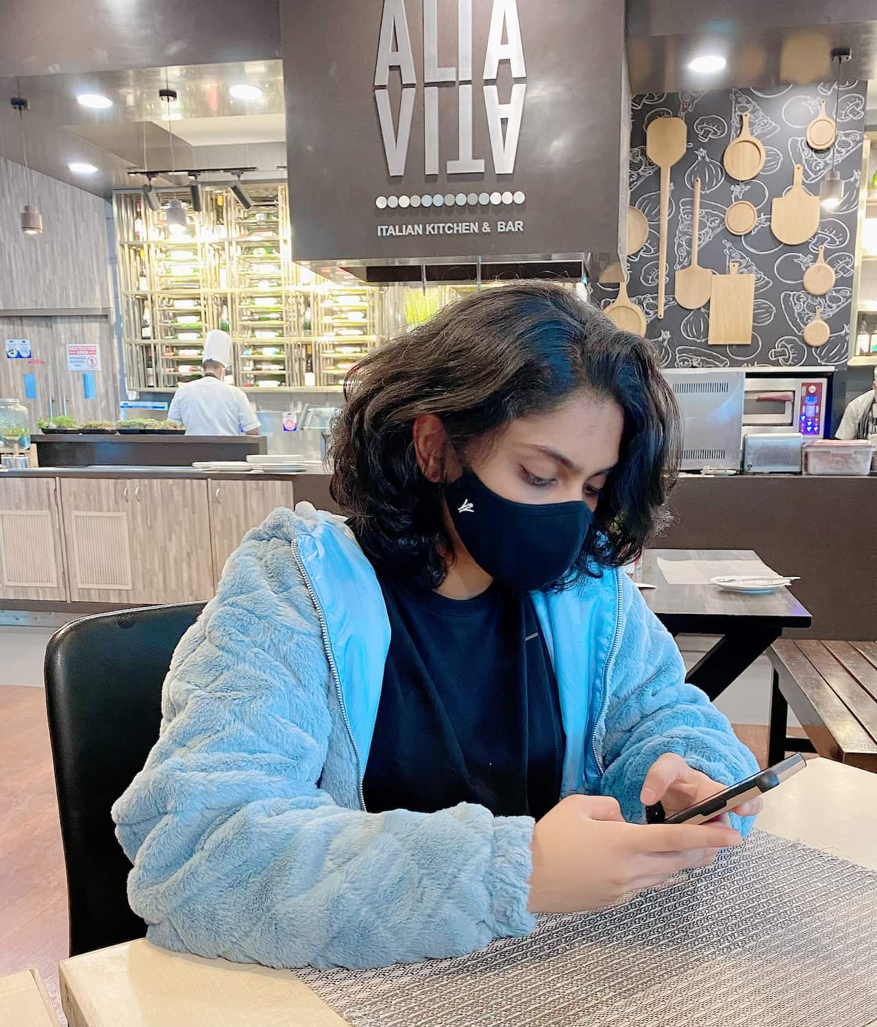 A woman wearing a face mask sits in a cafe while looking at her phone.