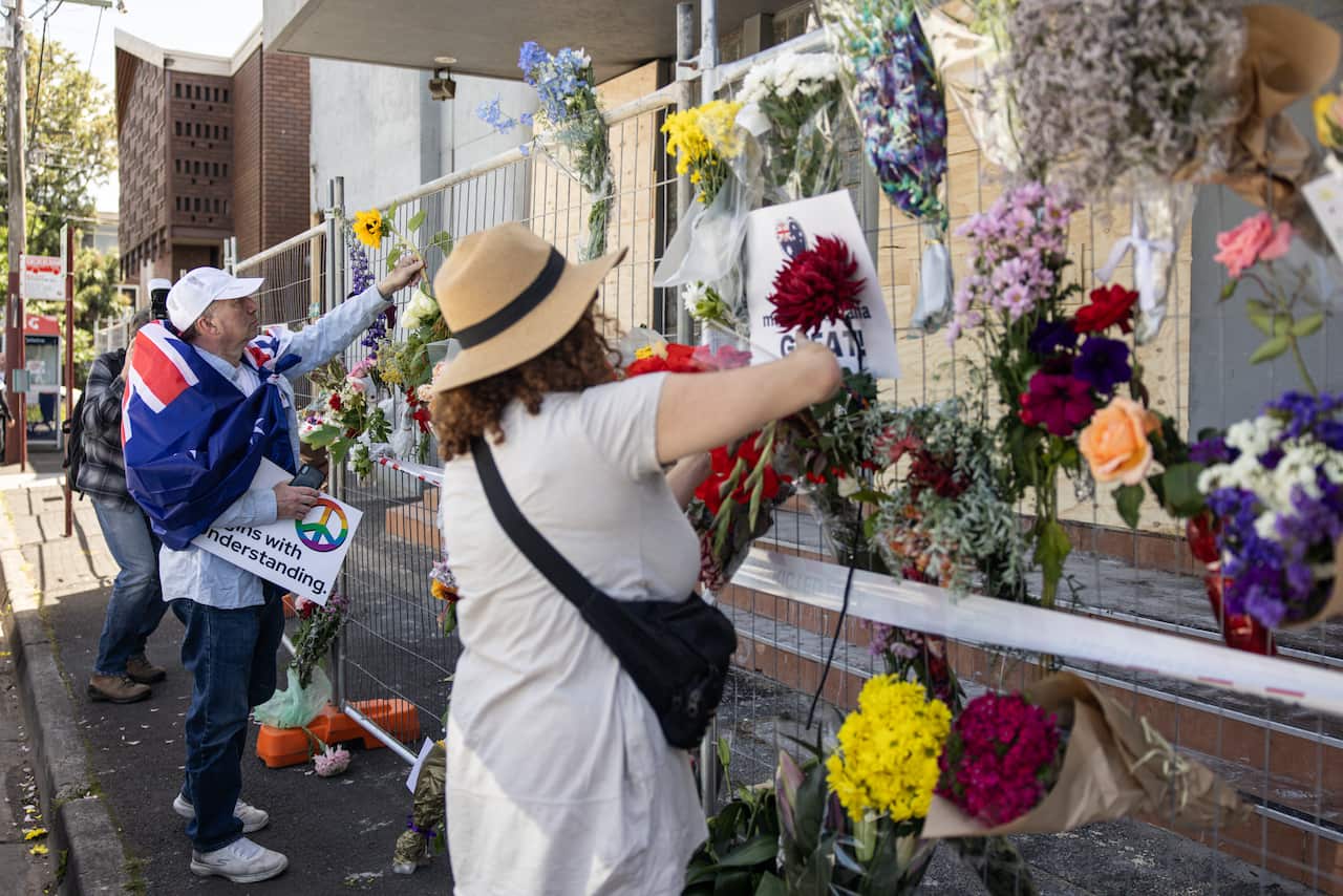 Two people placing flowers on a wire fence outside the synagogue.