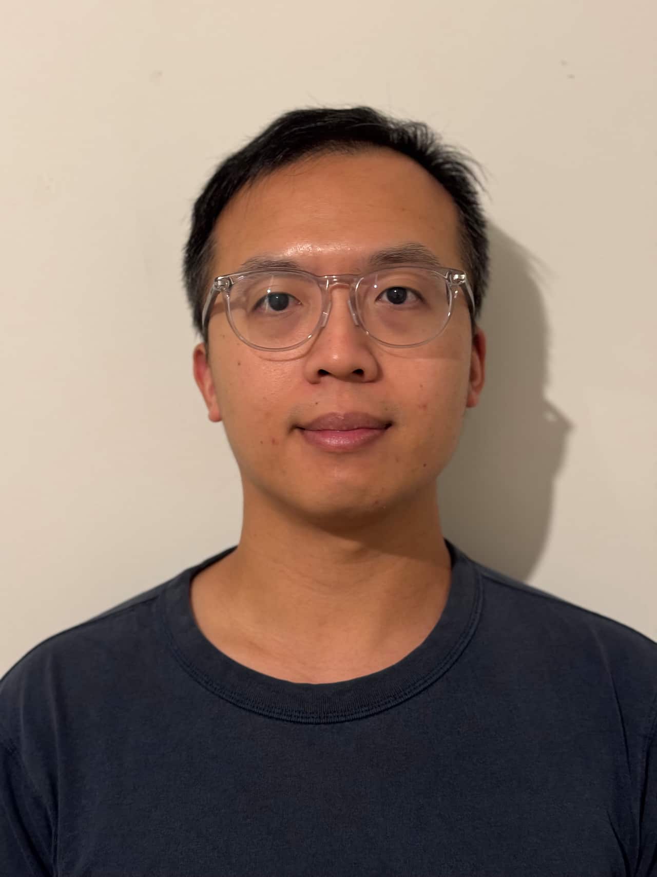 A headshot of a man in a black T shirt with a neutral expression on his face.