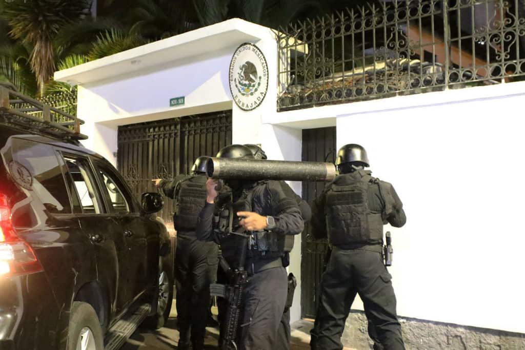 Rear view of  a small group of police special forces in black uniforms outside a compound with white walls 