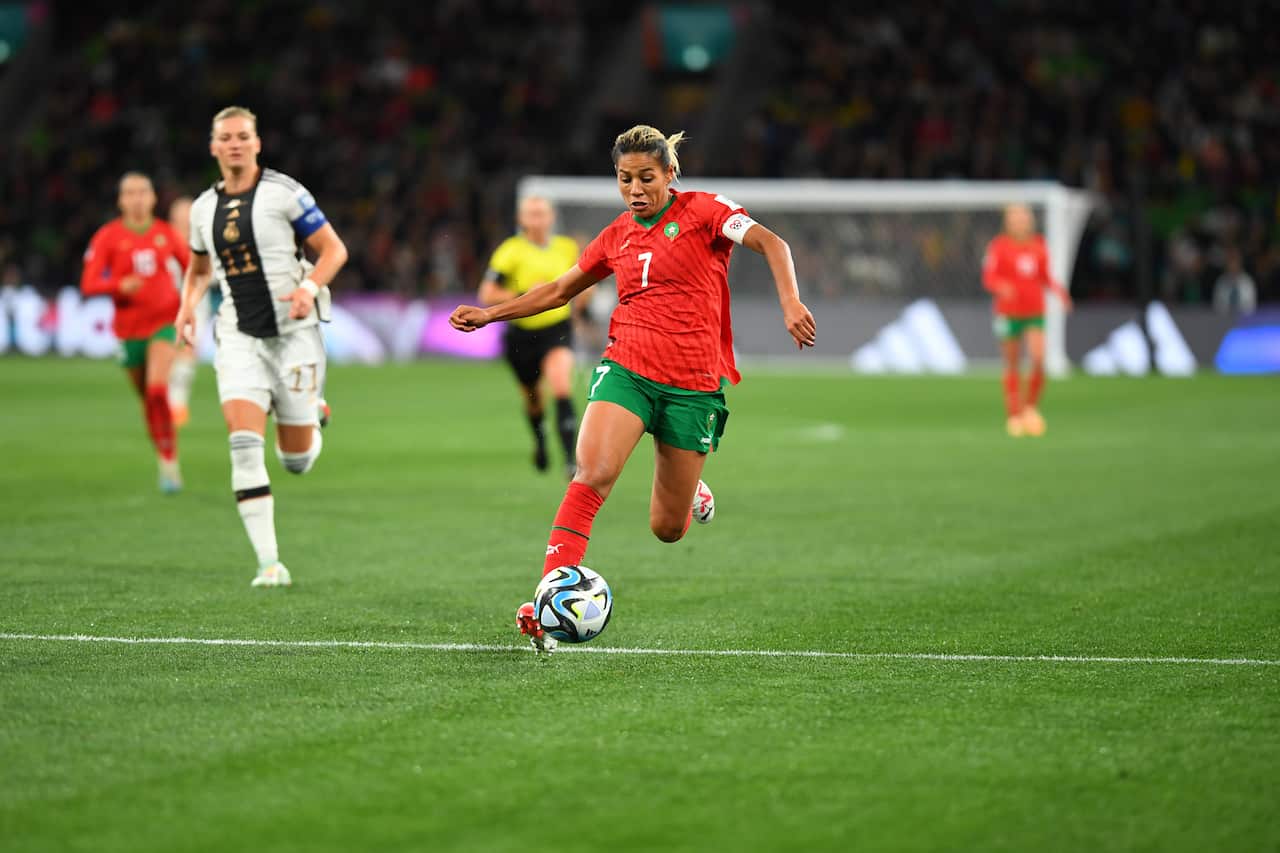 A woman in a red football uniform kicks a ball on grass.