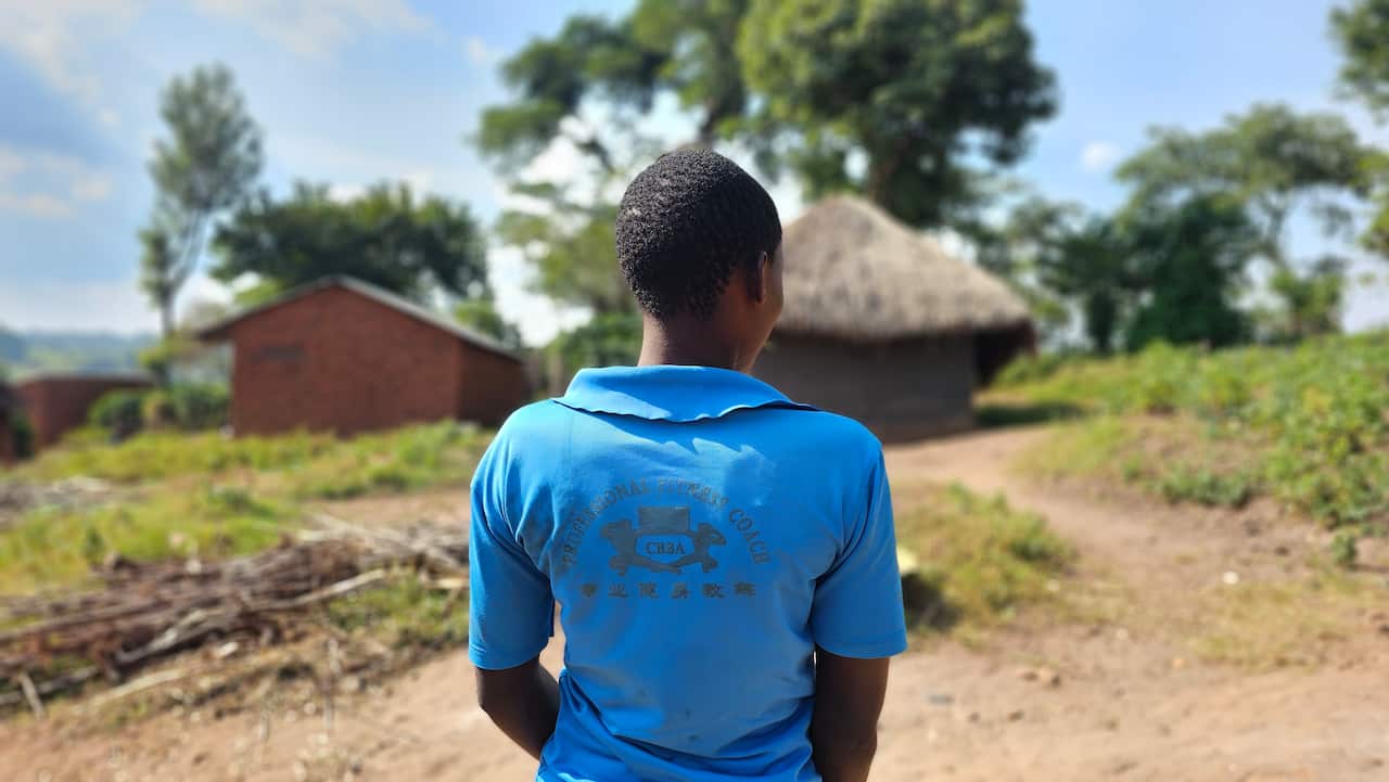 A photo of a Congolese woman wearing a bright blue shirt, facing away from the camera, outside
