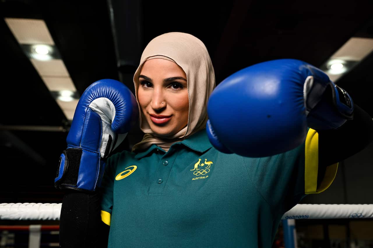 A woman in a hijab wearing a green polo shirt raising boxing-gloved fists