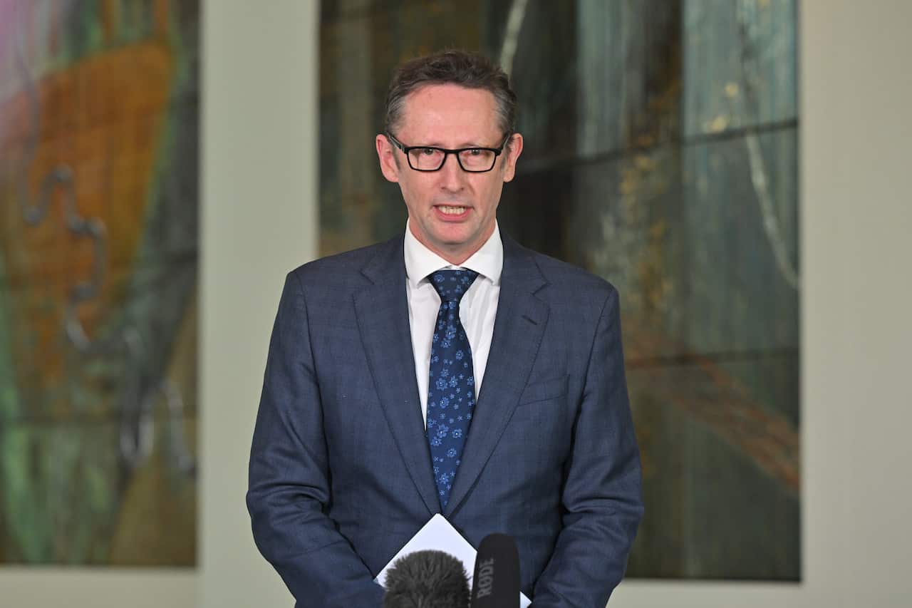 A man wearing a blue suit speaks into a microphone.