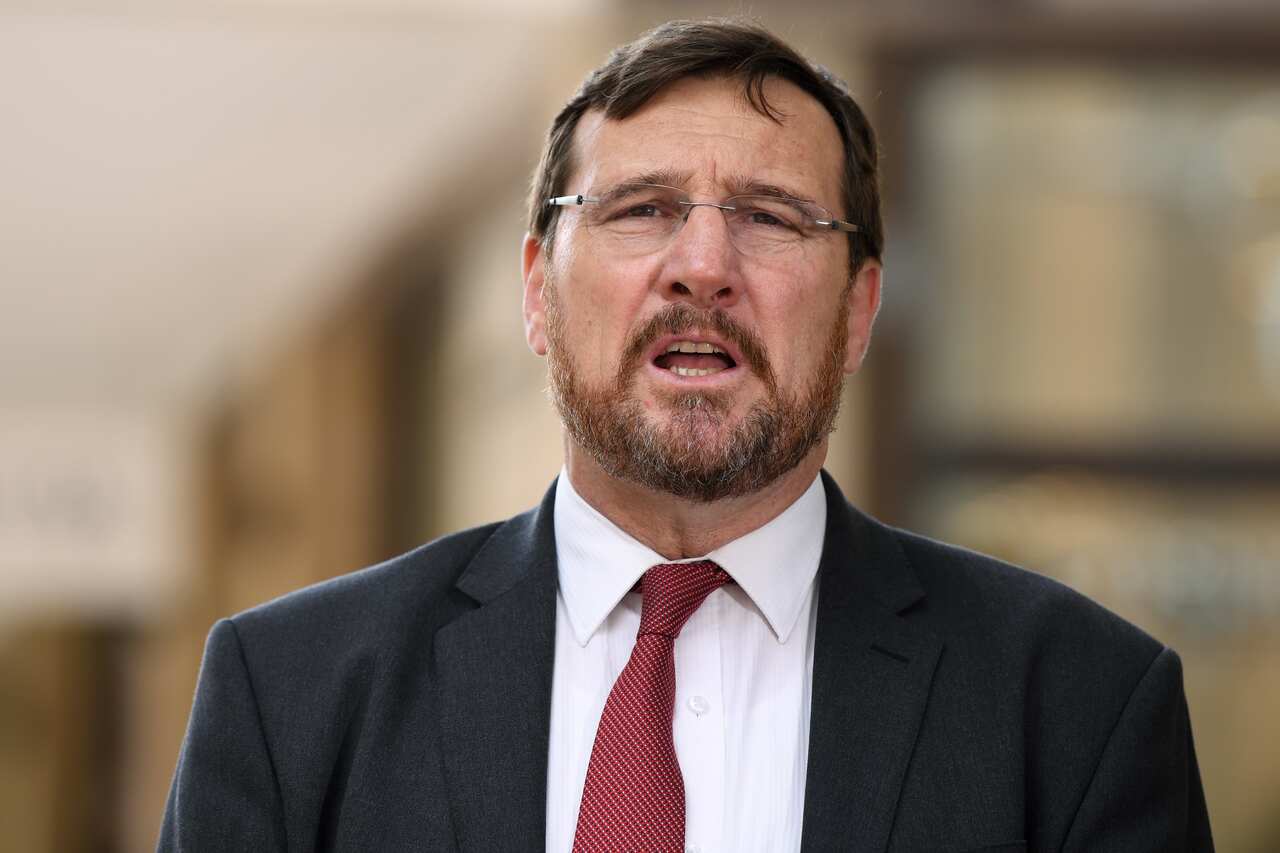 A man wearing a red suit and dark tie squints as he looks forward. 