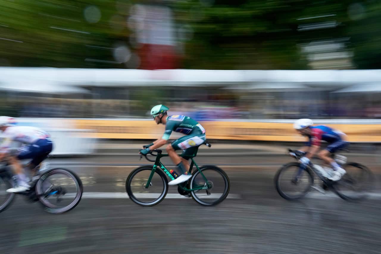 Side view of three cyclists on a road. The background is blurred