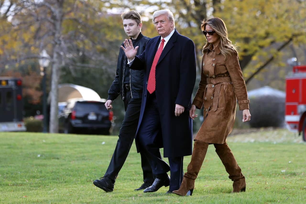 Donald Trump waves to the camera, walking alongside his wife, Melania Trump, on his left and his son, Barron Trump, on his right.
