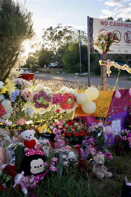 Teddy bears, stuffed animals, toys and colourful flowers are attached to a gate in front of a large sign that reads 'NO CAMPING'