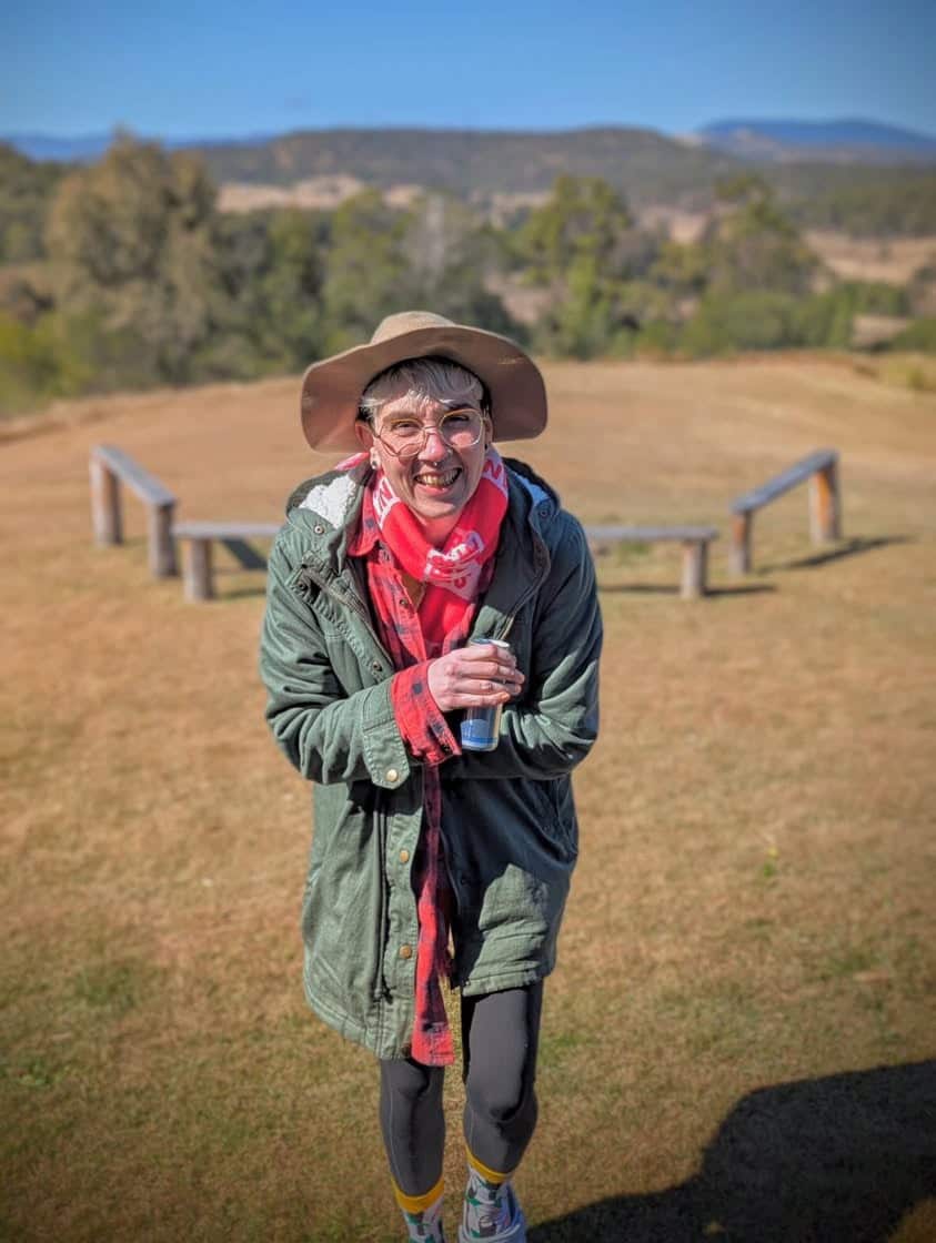 A person in an olive green jacket with glasses and a red tartan scarf