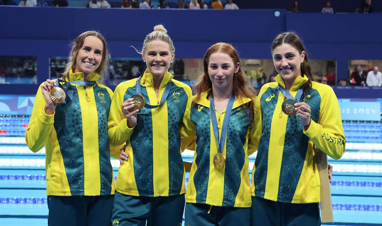 Four women stand holding medals next to a pool. 