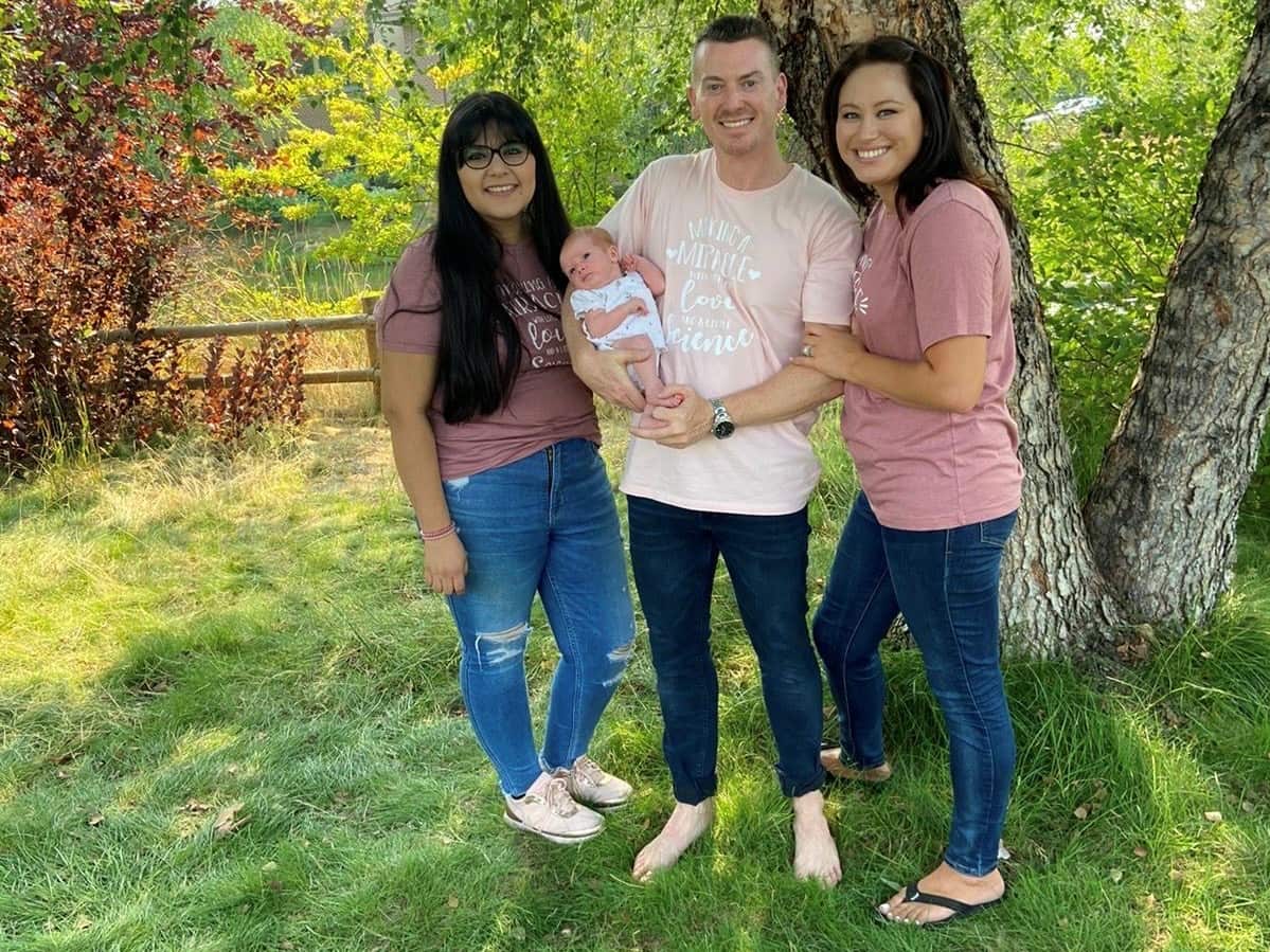 A man holds a baby standing between two women in a park.