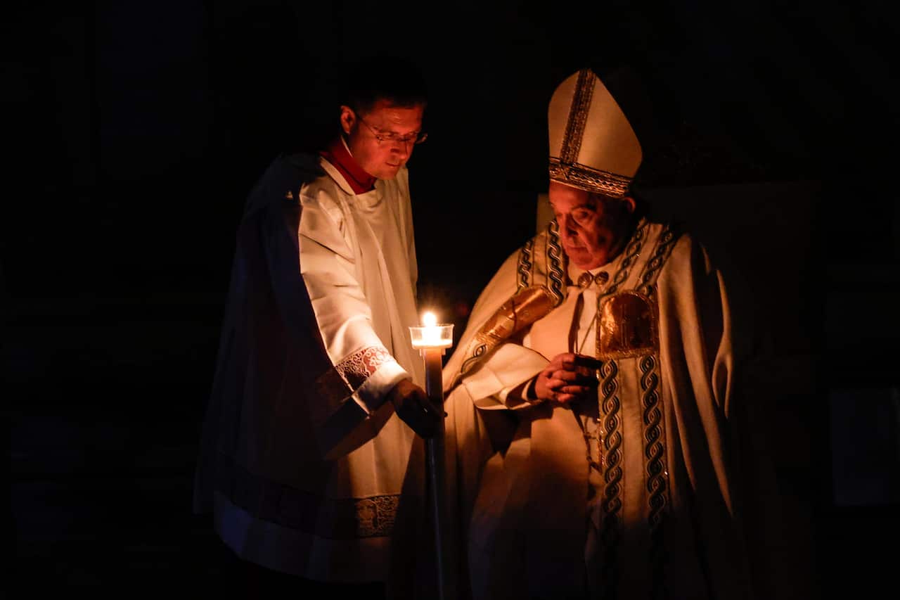 Pope Francis in the dark with a person holding a candle near him