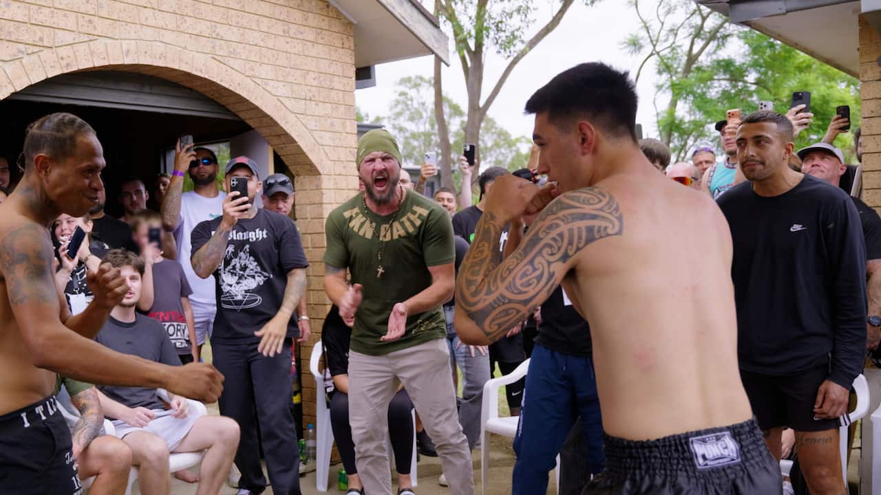 Two men step forward to fight, and a crowd cheers them on.