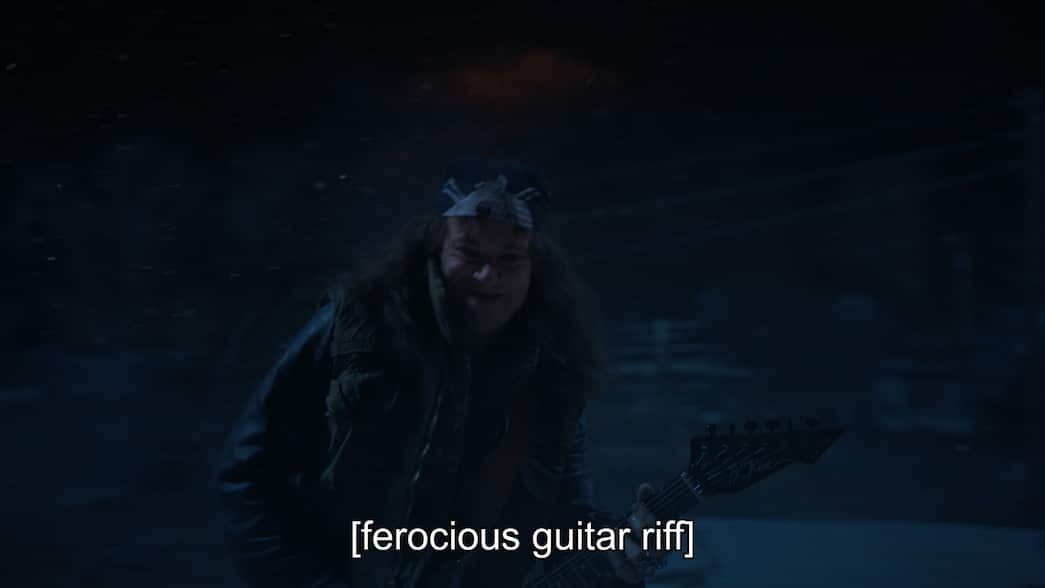 A man with long hair plays guitar with closed captions reading "ferocious guitar riff"