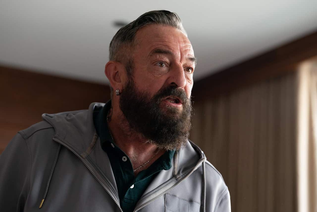 A bearded man leans forwared aggressively. 