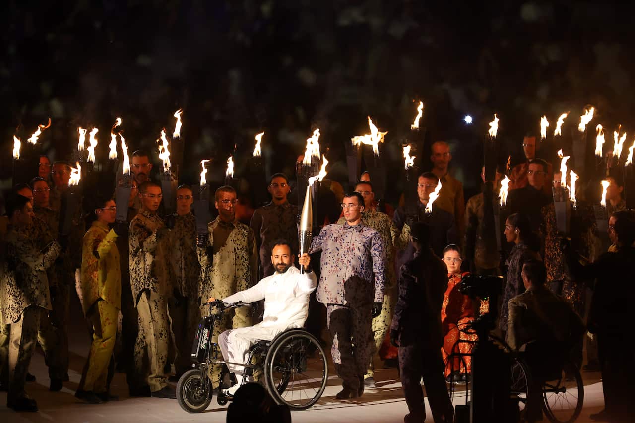 A person in a wheelchair holding up a torch. Others surround him also holding up small torches.