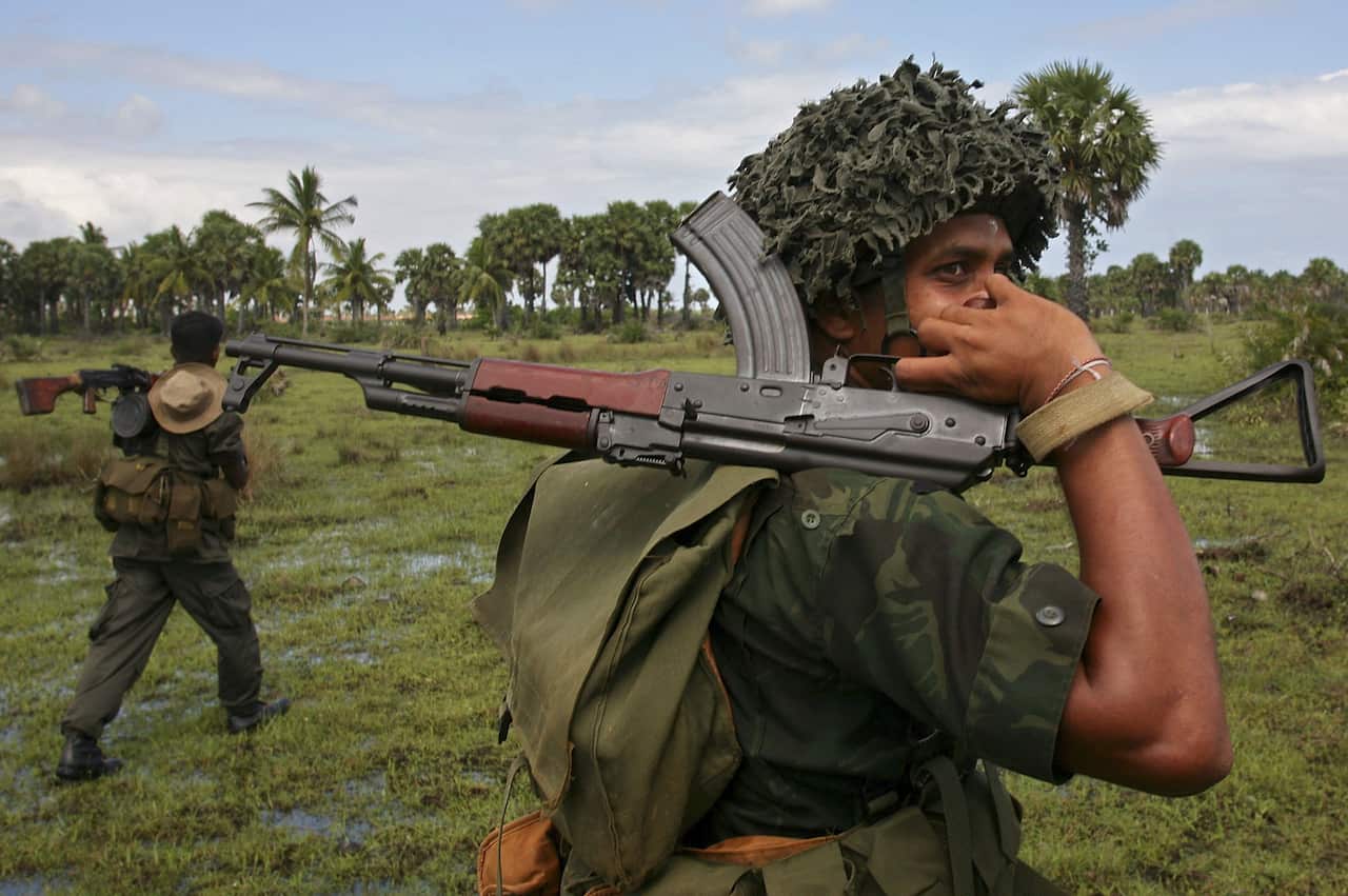 A soldier carrying a gun walks through marshland.