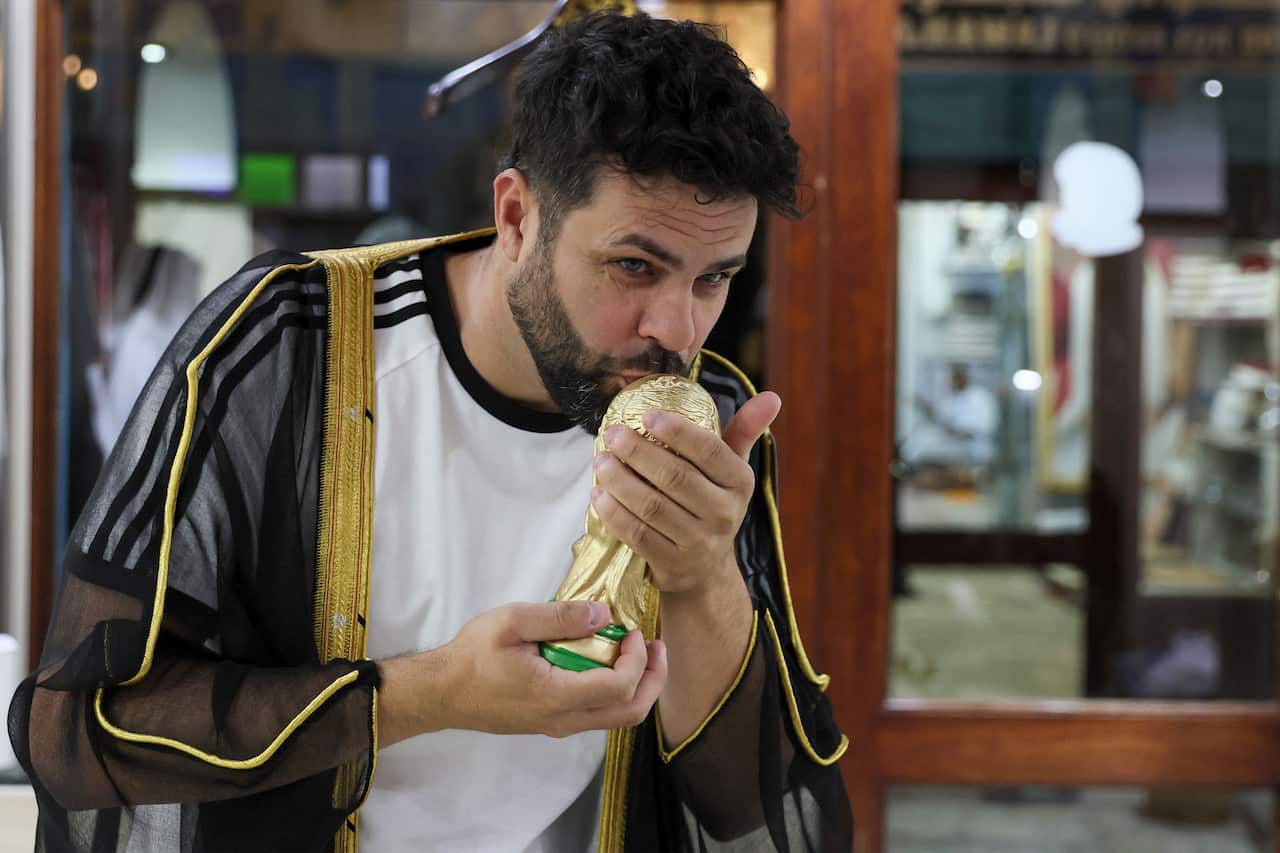 A man wearing a black and gold cloak kissing a mock World Cup trophy.