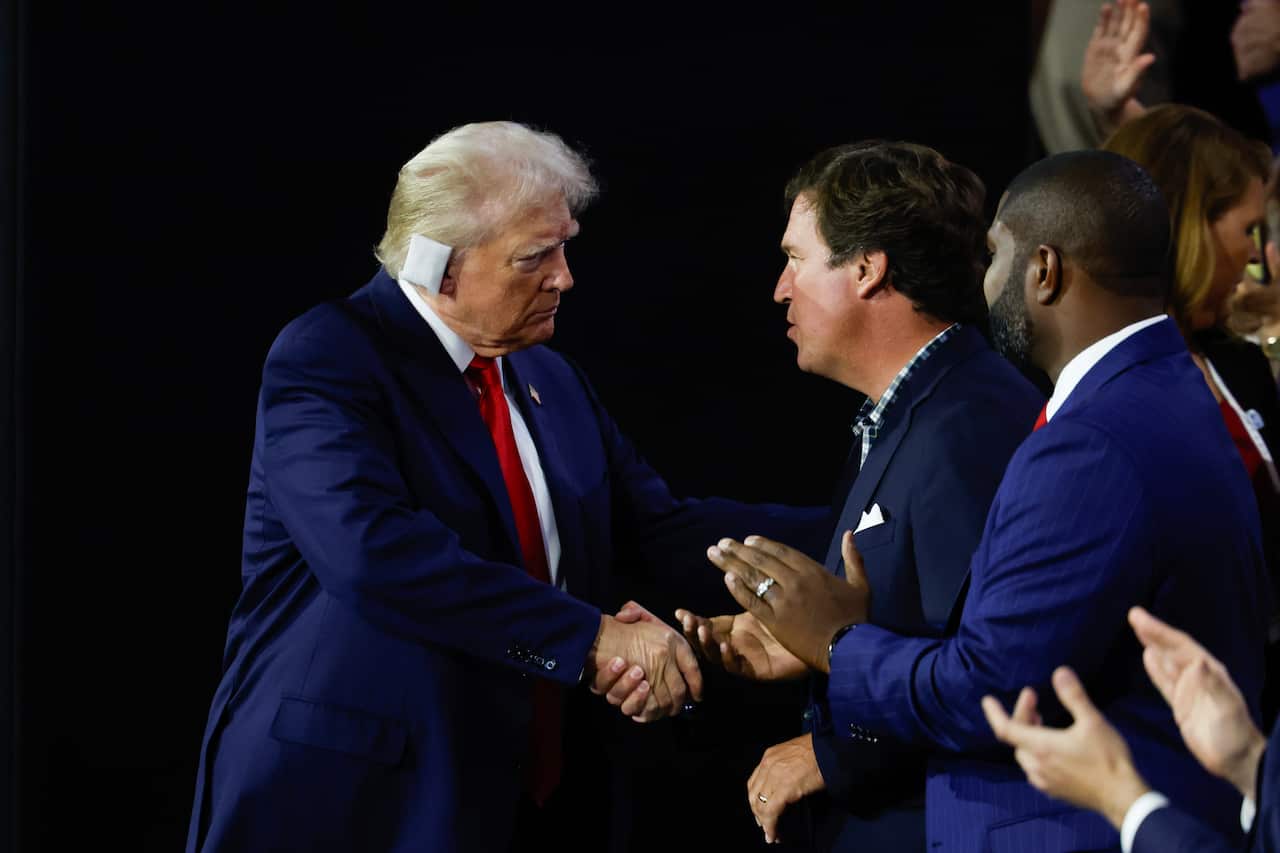 Two men shaking hands. One has a bandage on his ear.