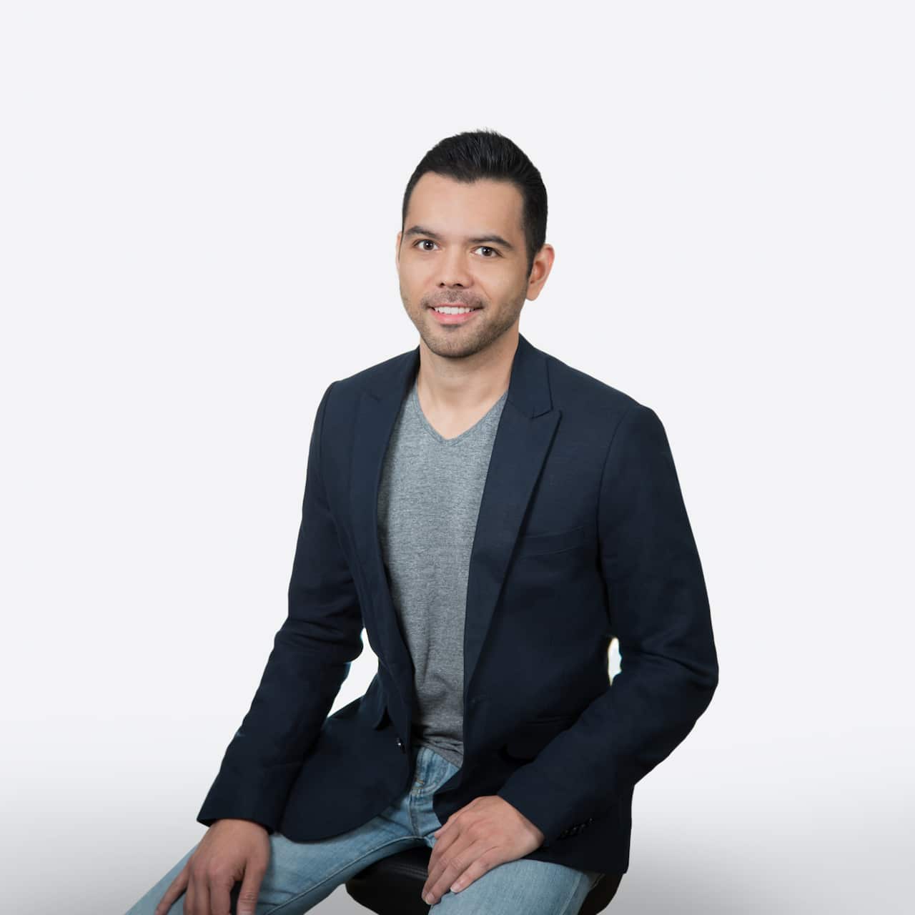 A man wearing a jacket and jeans sitting down 