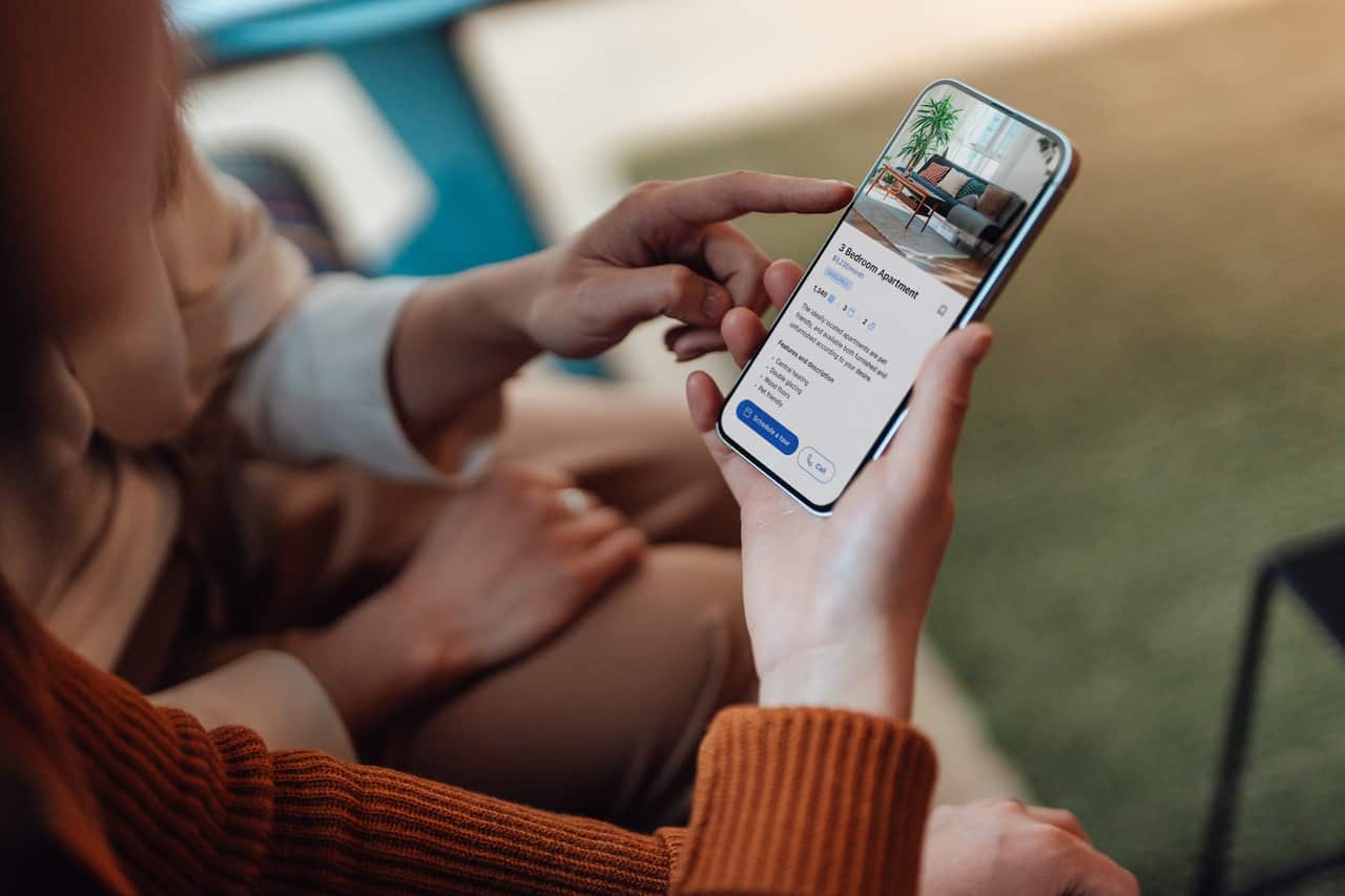 An over-the-shoulder view of a woman looking at a real estate listing on the smartphone.