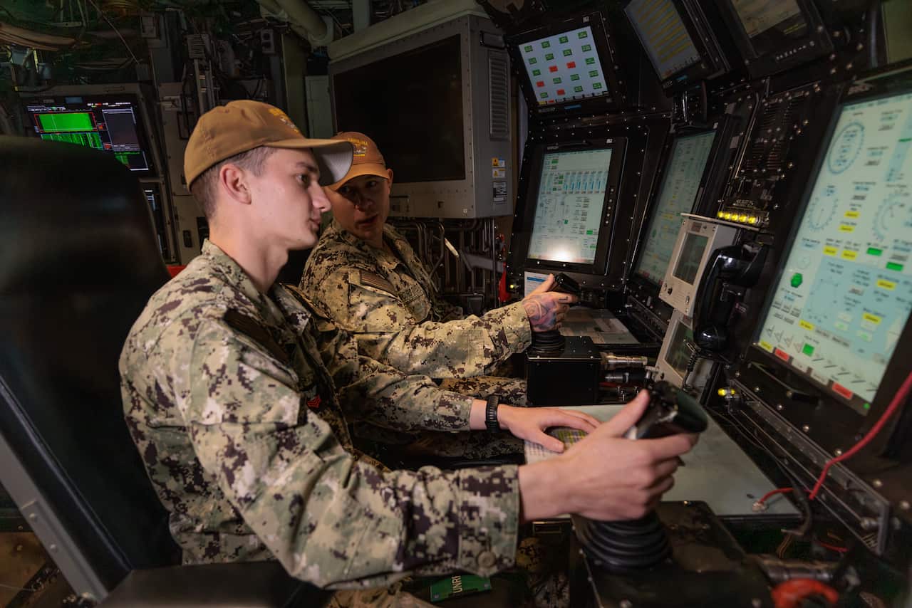 Inside a submarine two naval officers in full camouflage sit at their screens