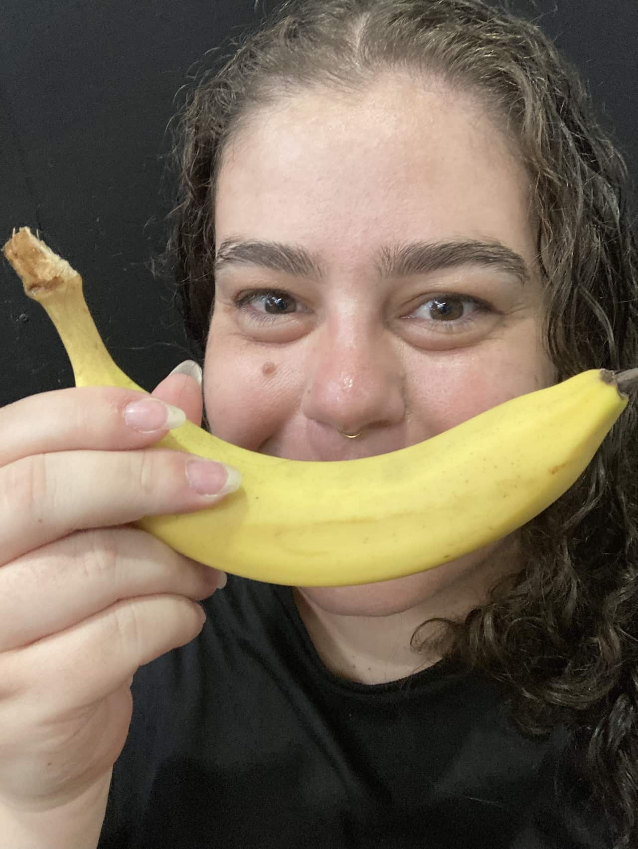 A woman smiling at the camera with a banana over her mouth in place of smiley lips.