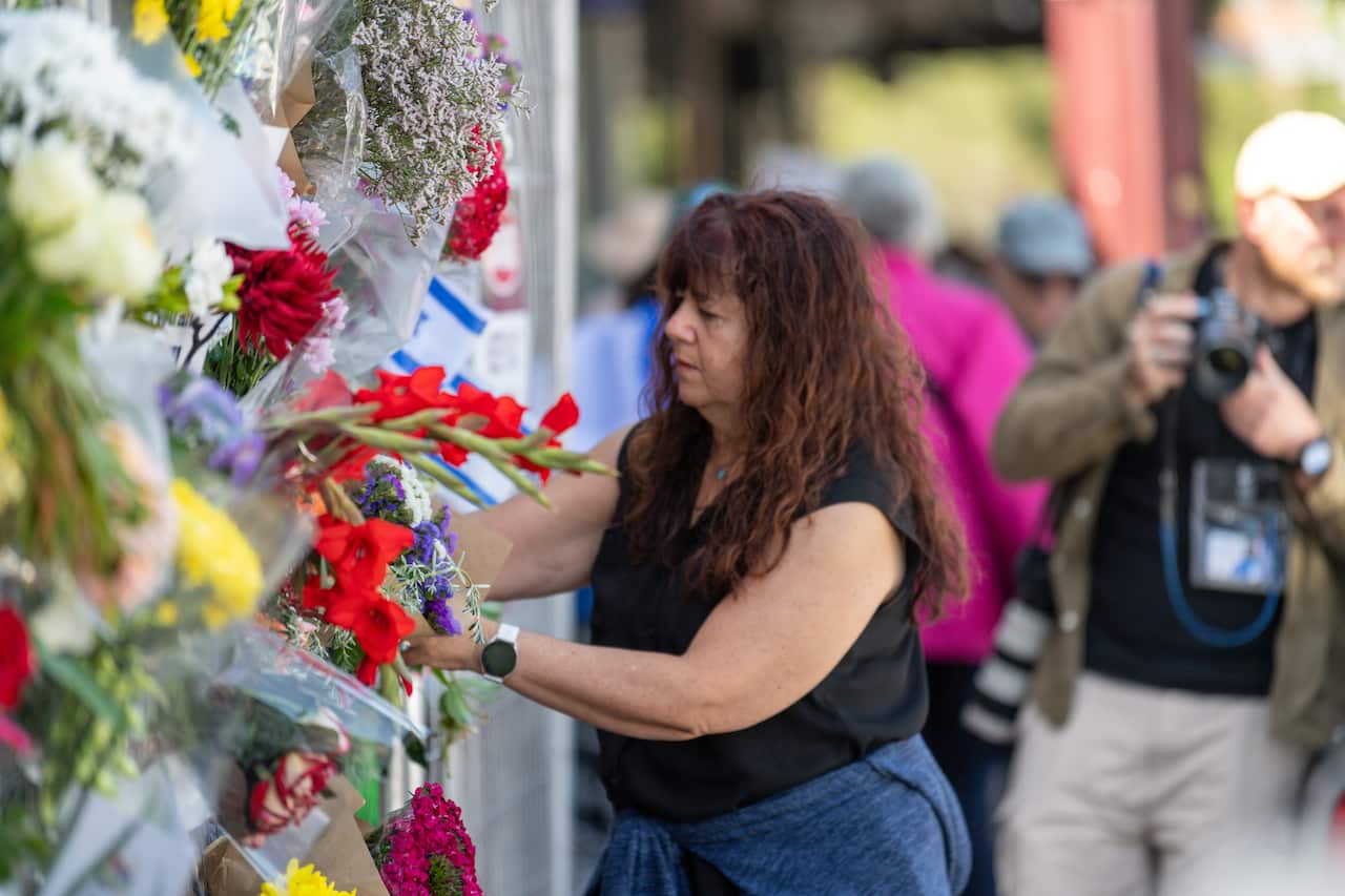A woman places flowers on a fence.