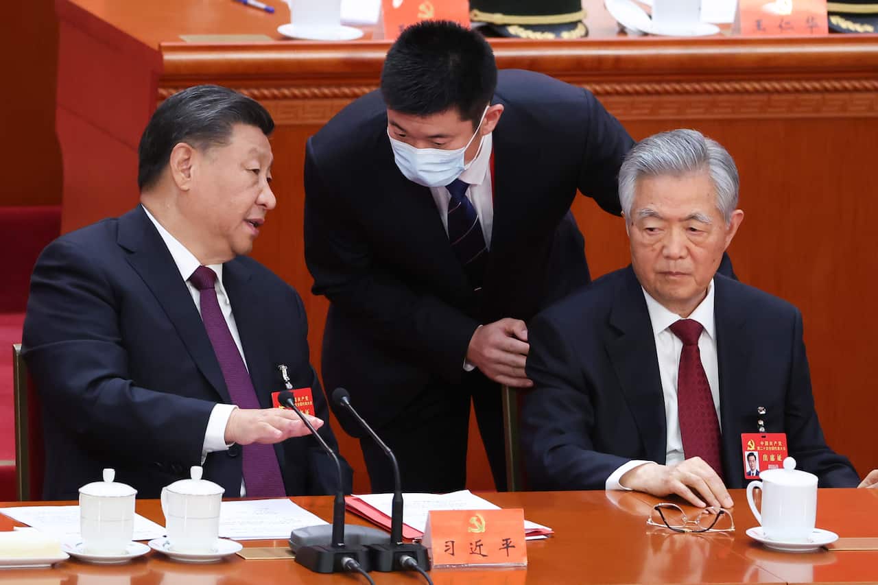 Chinese President Xi Jinping, sitting next to former president Hu Jintao, speaks with an official, who is standing at the National Congress Of The Communist Party Of China