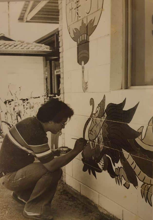 A black and white photo of a Chinese man painting a dragon on the outside of a building