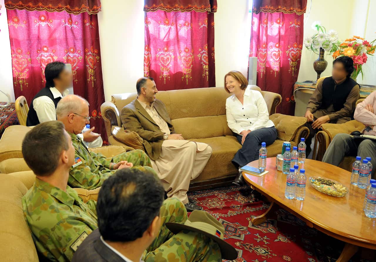 Man and woman talk on couch flanked by soldiers.
