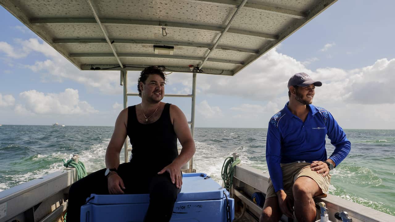 Alex and Shai, two young Malgana men, sit on the back of a fishing boat at sea.