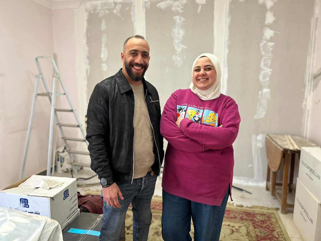 A smiling couple stand together in a room that's in the midst of being decorated.