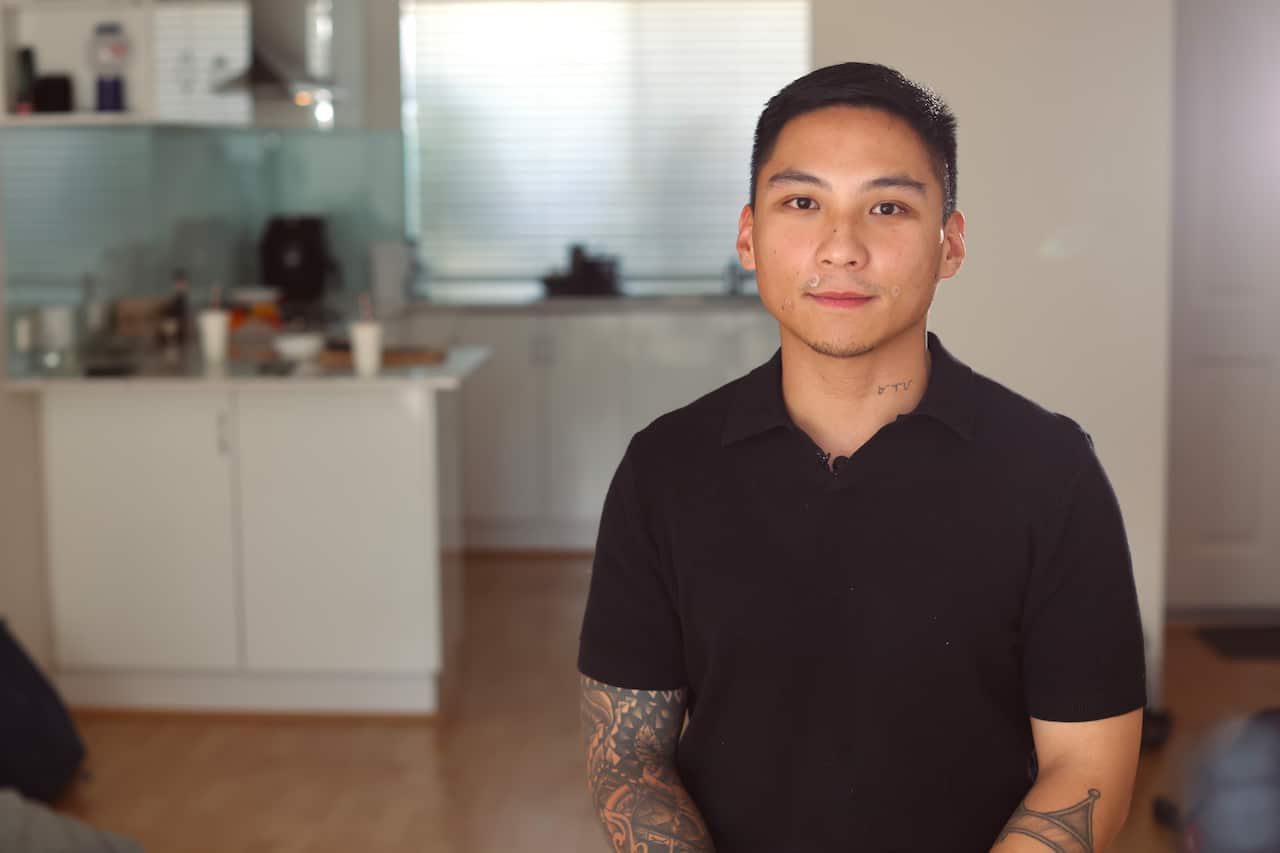 A young man wearing a black polo shirt sitting inside